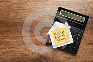 Paper note with words Mortgage Payment Holiday, house model and calculator on wooden table, top view. Space for text