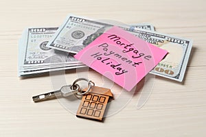 Paper note with words Mortgage Payment Holiday, key and money on white wooden table