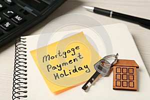 Paper note with words Mortgage Payment Holiday, key and notebook on white table, closeup