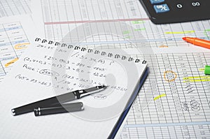 Paper notebook with accounting calculations and pen on the background of a table with numbers