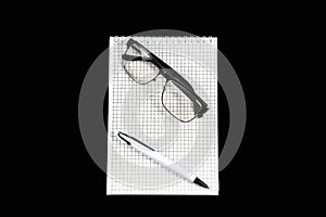 Paper notebook with ballpoint pen and optical glasses on black isolated background