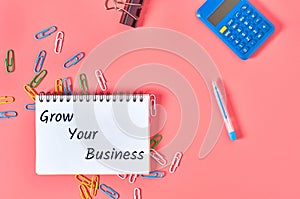 Paper notebook with words grow your business near stationery items on pink desk