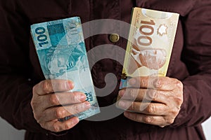 Paper notes from Canada and Brazil. Old retired person paying in cash