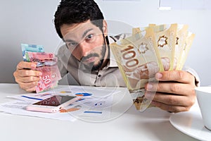 Paper notes from Canada. Dollar. Young adult holding many bills on table