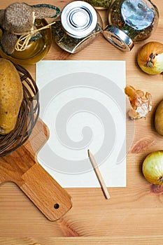 Paper, pencil, jug of olive oil, potatoes, onion, cutting board and spices