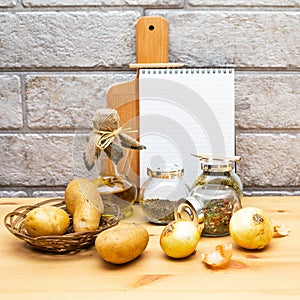 Paper, pencil, jug of olive oil, potatoes, onion, cutting board and spices