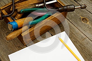 Paper with pencil and old tools in box on wooden