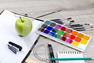 Paper, pencils, brush, green apple on wooden table