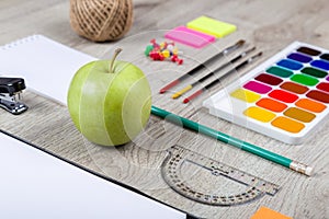 Paper, pencils, brush, green apple on wooden table