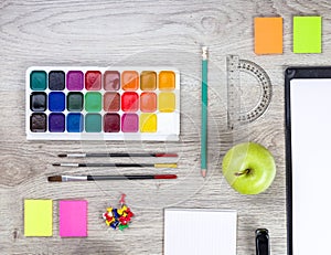 Paper, pencils, brush, green apple on wooden table