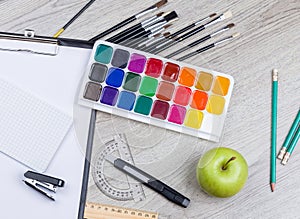 Paper, pencils, brush, green apple on wooden table