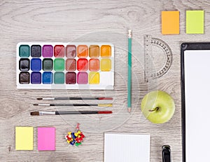 Paper, pencils, brush, green apple on wooden table