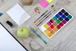 Paper, pencils, brush, green apple on wooden table