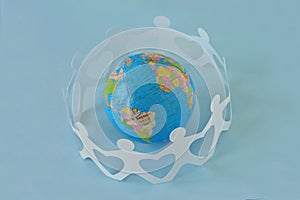 Paper people in a circle around earth globe on blue background -