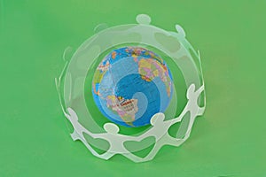 Paper people in a circle around earth globe on green background