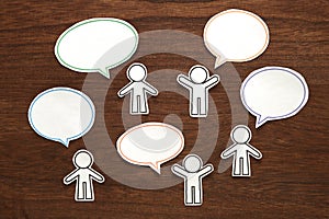 Paper people with colorful blank dialog speech bubbles on brown wood. Communication concept.