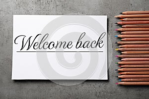 Paper with phrase Welcome Back and pencils on grey table, flat lay photo