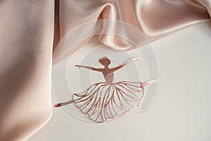 Paper pink ballerina performing a pirouette on a background of pink draped fabric