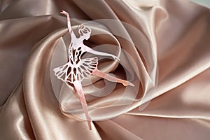 Paper pink ballerina performing a pirouette on a background of pink draped fabric