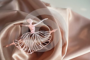 Paper pink ballerina performing a pirouette on a background of pink draped fabric