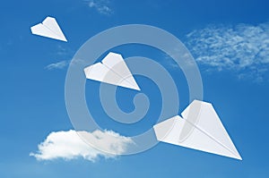 Paper plane flying over clouds with blue sky.