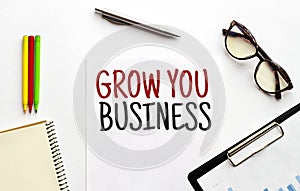 Paper plate, glasses, notepad,pen and pencils on the white background. Business concept. Text GROW YOUR BUSINESS