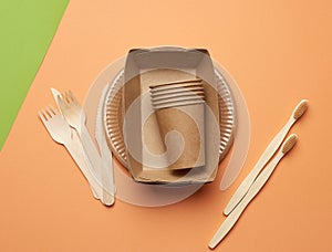 Paper plates and cups from brown craft paper and wooden forks and knive on a orange background