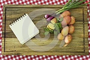 Paper for recipe on wooden board with potatoes, onion and parsnip leaves