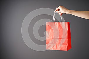 Paper red craft bag, eco packaging in a female hand on a gray background, space for text