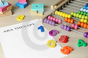 Paper sheet with abbreviation ABA Applied behavior analysis, abacus and colorful numbers on white wooden table