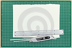 Paper sheet with metal ruler and utility knife on green cutting