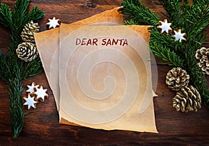 Paper sheet with text Dear Santa, between fir branches, cinnamon stars and pine cones on rustic dark wood, Christmas wish list or