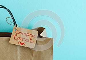 Paper shopping bag on a blue background. Label with heart and text COMPRA LOCAL. Shopping concept photo