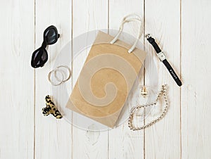 Paper shopping bag,sunglasses,watch,jewelry,hair accessories,parfume.Stiylish feminine accessories.Black and beige colors. Flat