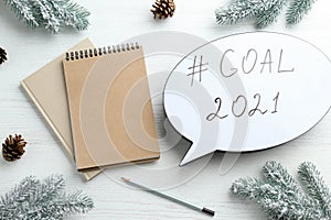 Paper speech bubble with hashtag Goal 2021, near notebooks and fir branches on white wooden table, flat lay. New year targets