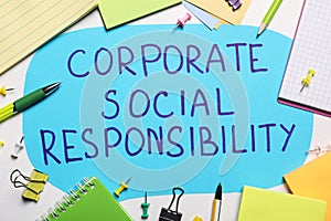 Paper text balloon with phrase Corporate Social Responsibility among office supplies on white table, flat lay