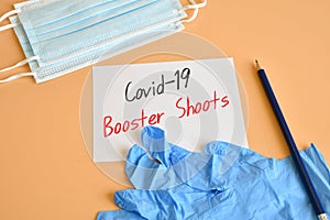 Paper with text `Covid-19 Booster Shoots` with protective masks and blue surgical gloves . Concept of combating the COVID-19 and