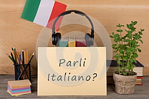 paper with text & x22;parli italiano?& x22;, flag of the Italia, books, headphones, pencils