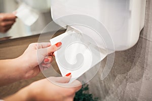 Paper towel dispenser. Hand of woman takes paper towel in bathroom.