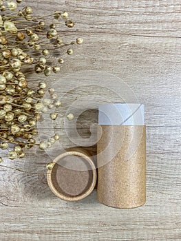 Paper tube with paper cover on wooden background with bouquet of dry flax. Flat lay concept. Top view. Vertical mobile
