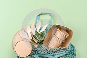 Paper utensils in blue cotton bag over light green background. Kraft paper cups, food containers