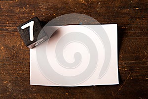 Paper and wooden cube with number on wooden table, 7