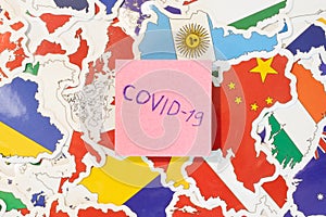 Paper with word Covid-19 flat lay top view on background with many national flags of countries. Concept of world healthcare