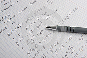 Paper with written mathematical calculations and pen, closeup