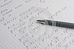 Paper with written mathematical calculations and pen, closeup