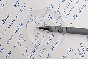 Paper with written mathematical calculations and pen, top view