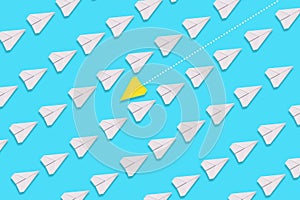 A paper yellow airplane is flying against the general direction of the white airplanes. Blue background. Flat lay. The concept of