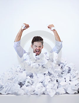 The paperwork keeps piling up around him. A young businessman buried in paperwork showing his frustration.