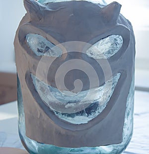 Papier mache mask on a glass jar. Handmade paper and dough.