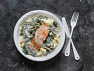 Pappardelle pasta with creamy spinach mushrooms sauce and baked salmon on a dark background, top view. Salmon florentine homemade